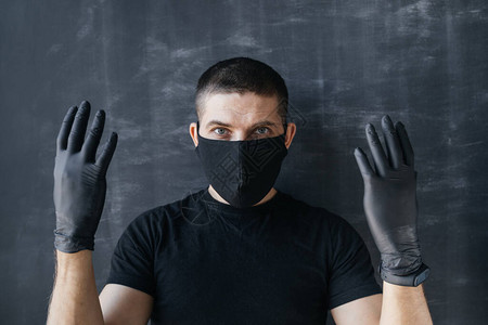 一个戴着黑色面具和医用手套的男人在黑暗的背景下展示了他的双手验尸官流行病保背景图片