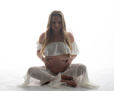 怀孕的妇坐在白背景上时抚摸肚子而她却图片