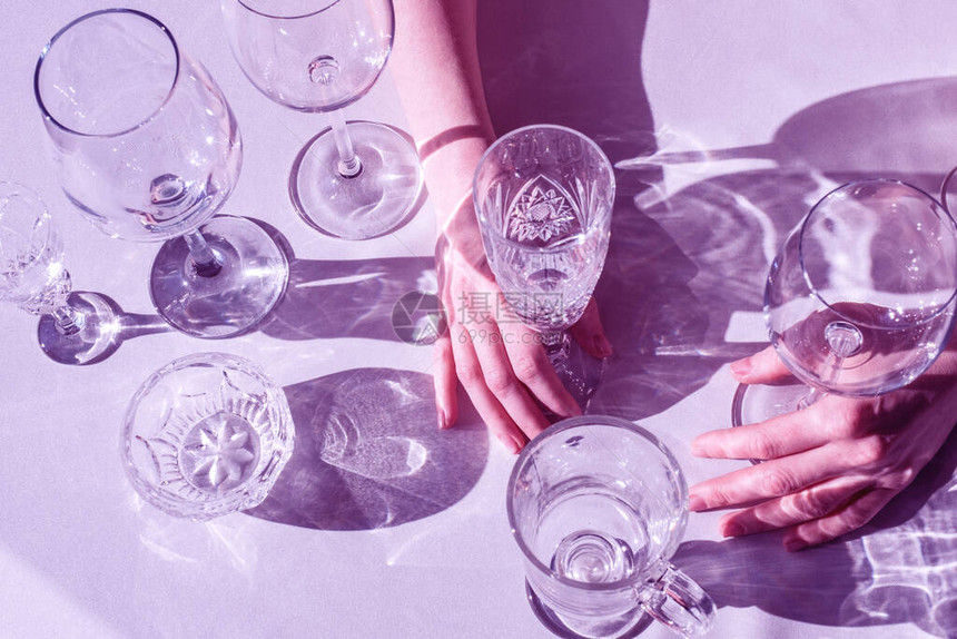 女人的手在霓虹紫色背景的桌子上放着不同的酒杯很多玻璃杯的饮料图片