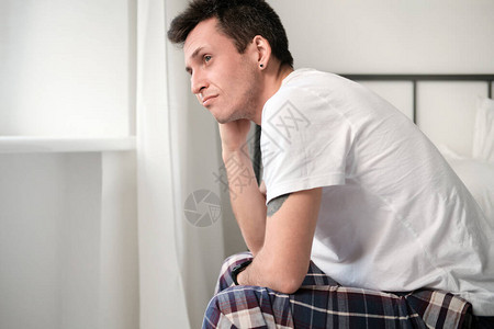 穿着白衬衫和睡衣的年轻人坐在床上高清图片