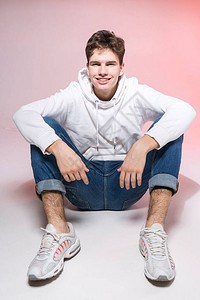 时尚英俊的年轻欧洲男模特身着白色运动衫蓝色牛仔裤和白色运动鞋背景图片
