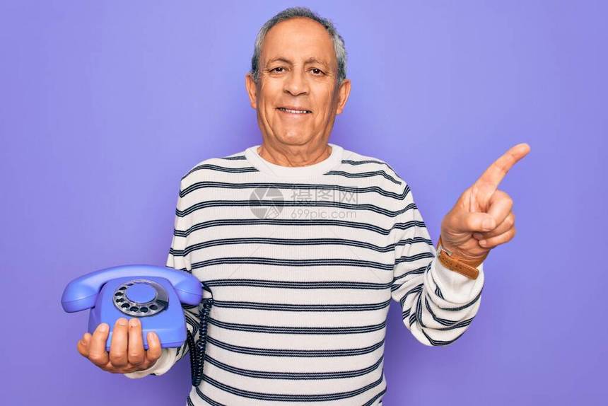 高级英俊的灰色长发男子拿着古老的听筒电话在紫色背景上非常快乐用手和图片