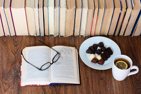 打开课本眼镜白盘上的茶和巧克力糖木桌上的一摞旧书教育理念背景许多书堆图片