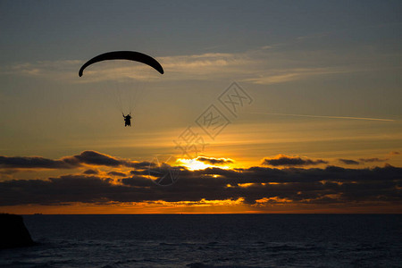 滑翔伞在阴云的日落下飞越海岸图片