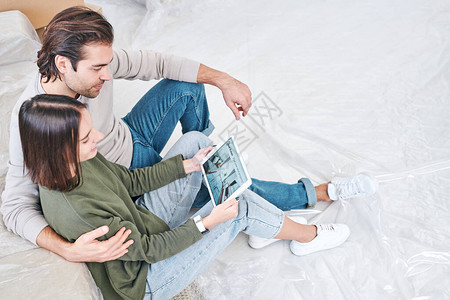 带着触摸板的年轻可爱夫妻透过网上观摩沙发新公寓规划的想法图片