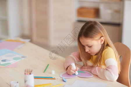 可爱的小女孩在舒适的室内坐在餐桌旁为母亲节制作手工卡片的高角度肖图片