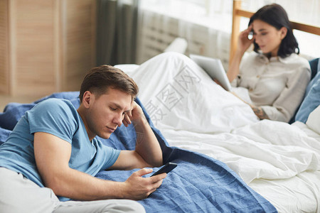 现代年轻夫妇坐在床上时使用移动设备通信问题概念复制空间的近代年图片