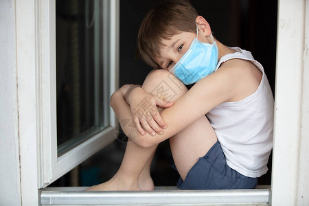 一名身戴医疗面具的儿童坐在窗帘上图片