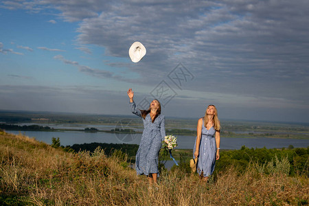 两个快乐的年轻女孩穿着蓝色夏服沿着河边草地高岸行走享受野生未图片