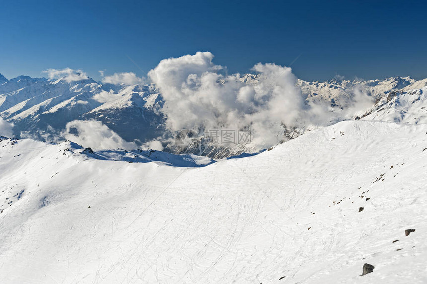 在高山脉的冰雪覆盖山谷下以蓝天空背景和云图片