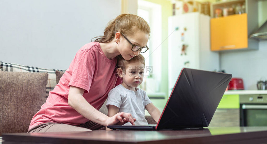 一名膝上有一个小孩的年轻妇女坐在一台笔记本电脑上图片