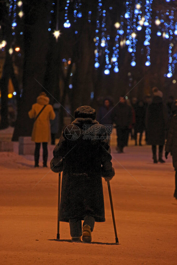一位依赖两根棍棒的老年妇女在圣诞节穿过一个冬季公园图片