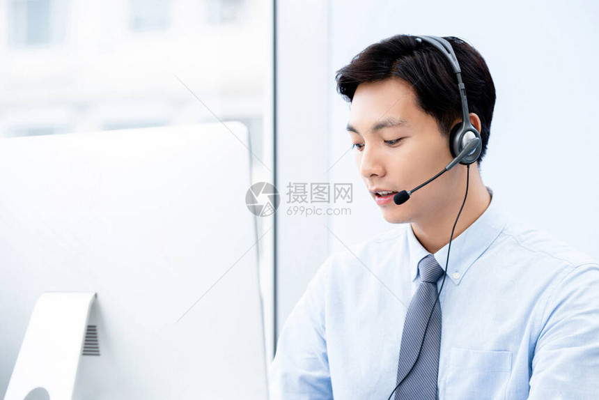 年轻英俊的男亚洲人呼叫中心的代理在办公室里看电脑工作的图片
