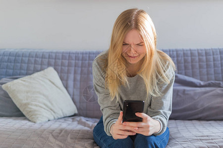 一个悲伤的金发女人坐在家里客厅的沙发上查看电话的前视图技术概图片
