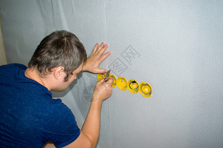 男人用刀把插座的墙壁上的壁纸切开图片