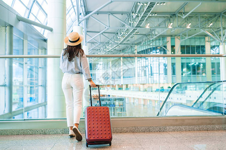 带着行李在国际机场走着的年轻女子在机场休息室等待飞行机的图片