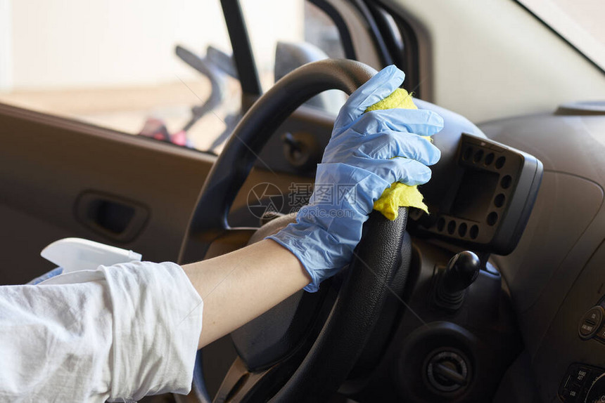 戴着橡胶防护手套消毒汽车方向盘的女人清洁车辆内部以防止冠状图片