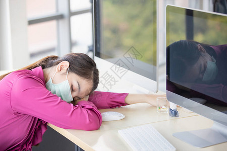身戴卫生保护面罩的女雇员在办公室工作并感到发烧后疲劳摔倒和睡在桌子上图片