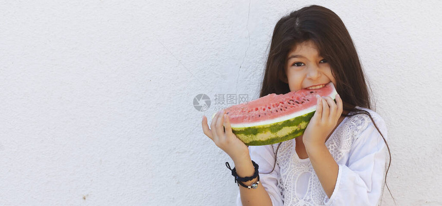 一个美丽的少女在户外吃西瓜的画像一个小女孩手里拿着一大片又甜多汁的西瓜面部表情感觉快乐有趣俏皮和图片