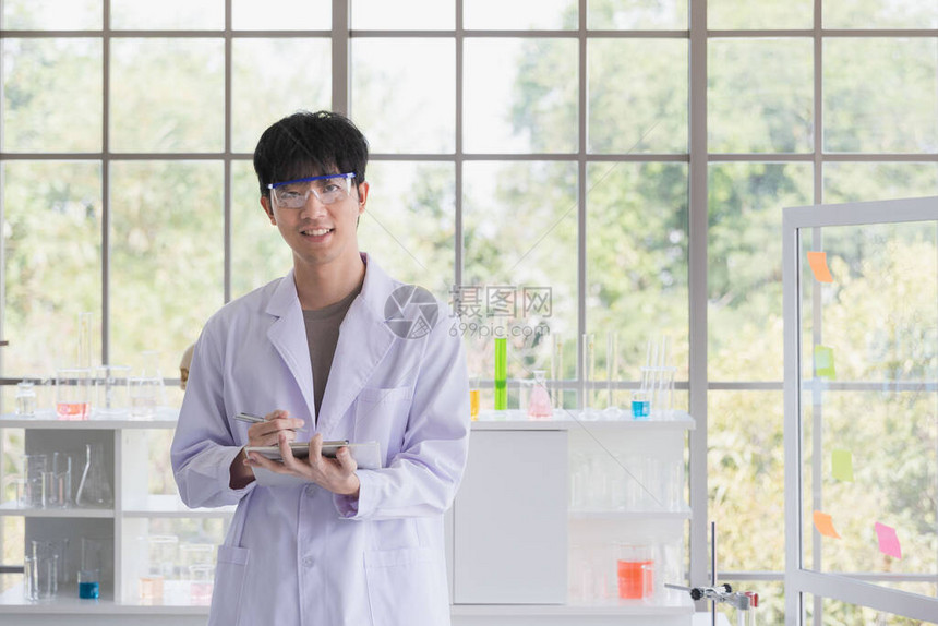 亚洲男科学家站在实验室里摆姿势和看镜头在他身后的架子上有丰图片