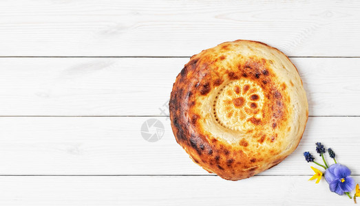 白色木制背景上的美味新鲜圆形泥炉面包图片