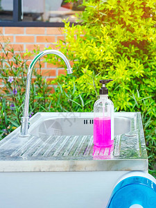 花园铝水槽上的粉色酒精凝胶瓶或抗菌肥皂消毒剂图片
