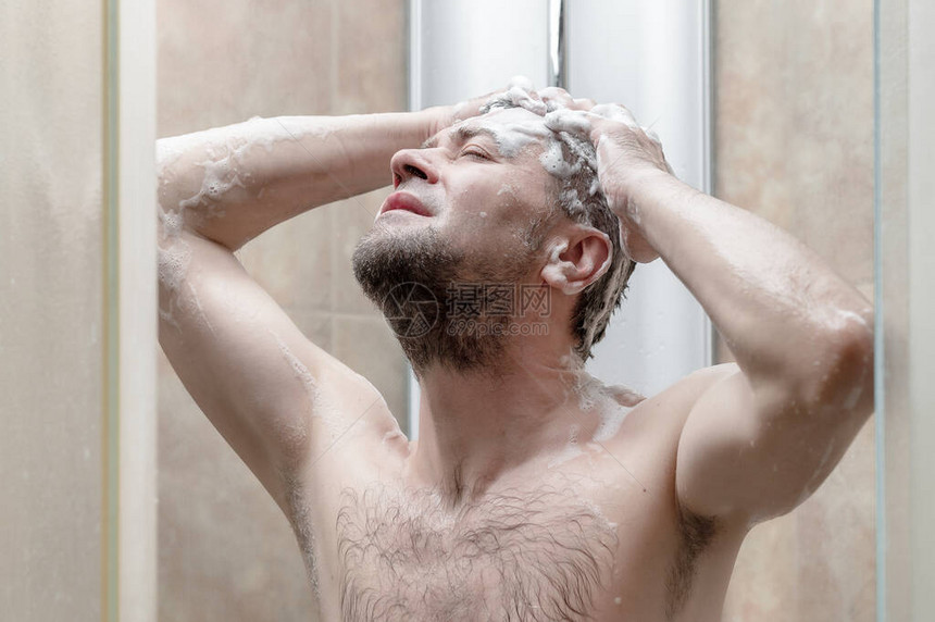 男人在现代瓷砖浴室的淋浴间里洗头图片