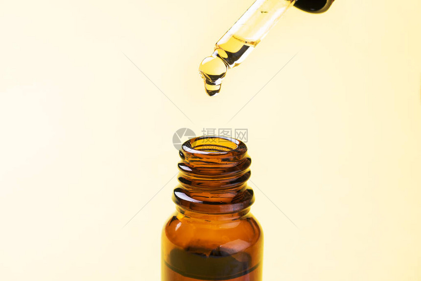 液滴从移液管中落下在黄色背景上带吸管的一瓶化妆品油复制空间图片