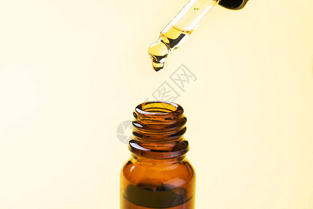 液滴从移液管中落下在黄色背景上带吸管的一瓶化妆品油复制空间图片