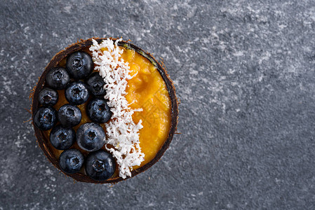 深色背景的椰子碗中冷冻芒果蓝莓和椰子泥的顶视图冰沙甜点图片