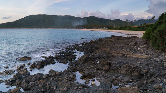 菲律宾帕拉万州埃尔尼多附近的纳克潘海滩火山岩滩云层和棕榈树边海图片