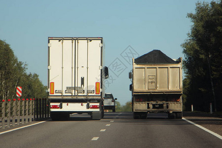 带白色货车拖的半卡车在郊区高速公路上超越装载的平板自卸车图片