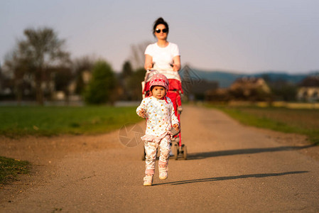 年轻母亲和幼儿在红色婴儿车前面跑图片