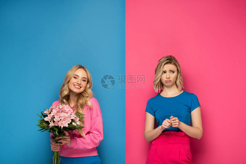 美丽的金发女孩微笑着拿花束靠近粉红色和蓝色背景的图片