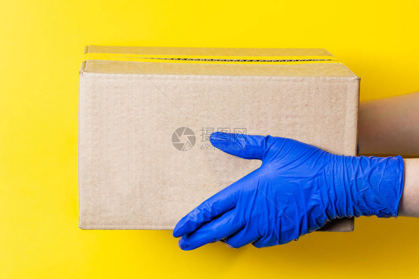 一个戴着医用乳胶手套的男人在黄色背景上递送一个包裹冠状大流行期间安全运图片
