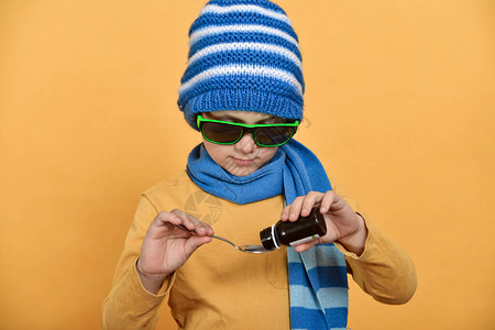 戴蓝帽子和围巾的男孩倒药和瓶子治疗感冒图片