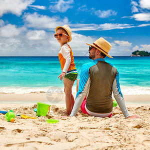 抗癌卫士3岁的小孩男和父亲一起在海滩上度假在塞舌尔背景