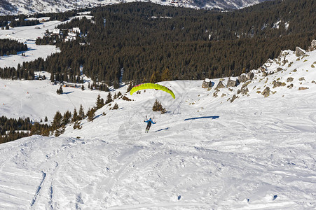 滑翔伞从雪地覆盖的斜坡上起降向高山图片