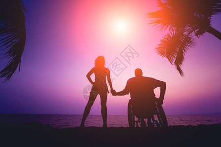 与妻子一起坐在轮椅上的残疾男子在海滩上图片