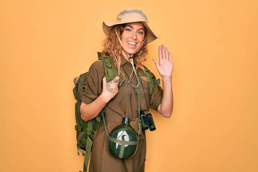 穿背包和水壶的蓝眼睛徒步旅行的金发年轻探险家女青年躲在一边打招呼快乐微笑图片