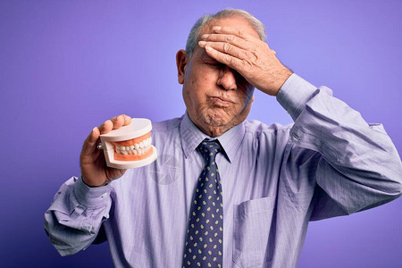 头发灰白的老人在紫色背景上拿着正畸假牙图片