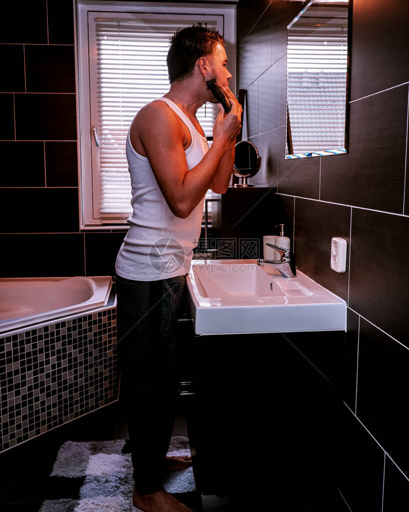 欧洲男人在浴室里用电动设备剃须图片