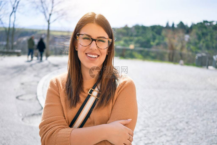 年轻美丽的黑发女人戴着眼镜微笑着快乐而自信站在城市街道图片