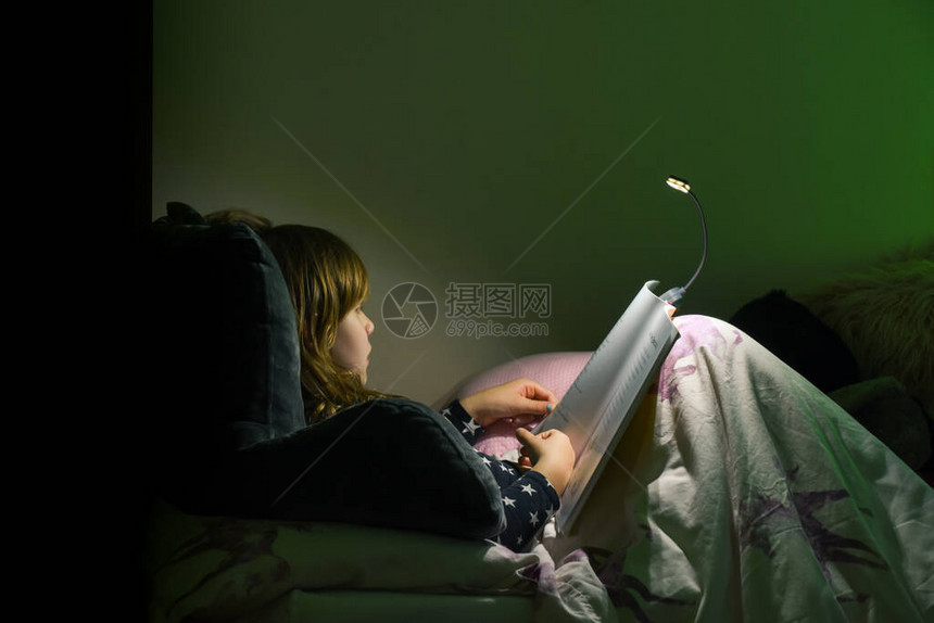 女孩晚上在睡床上看书在舒适的卧图片