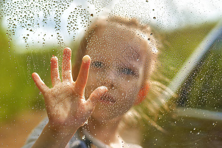 金发女孩画着一个湿润的窗户玻璃上有雨滴图片