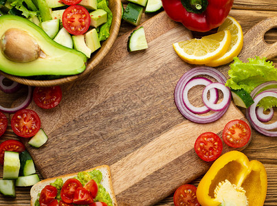 新鲜的五颜六色的蔬菜和健康的烹饪原料围绕着空木菜板背景图片