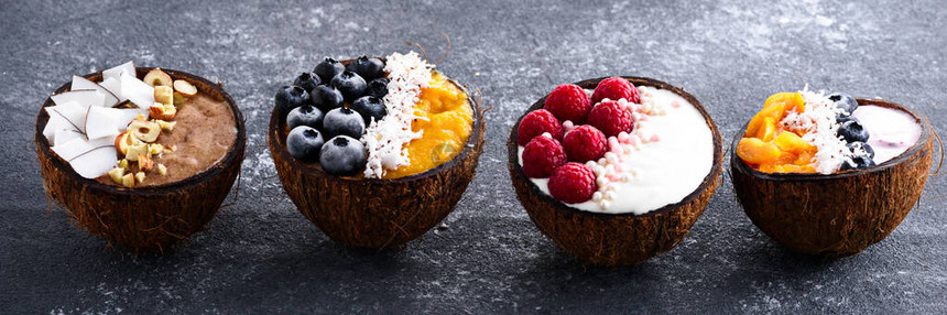 在灰色背景的椰子碗中特写四个带有浆果和水果的冰沙碗图片