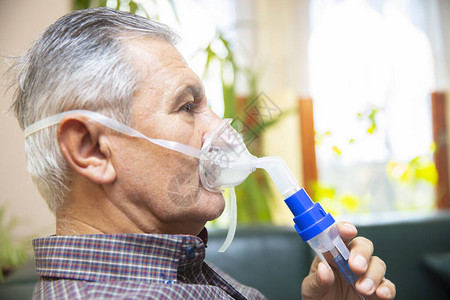 高级男子使用医疗设备吸入呼吸道面具室内喷雾器的图片
