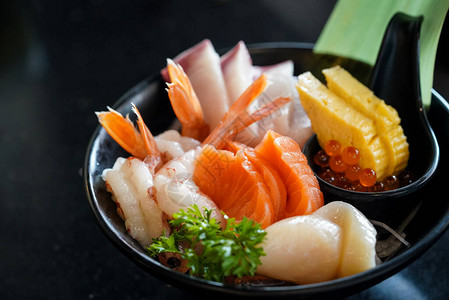 生鱼片套装精美地排列在饰有绿叶的黑色盘子中日本料理自助餐主厨推荐图片
