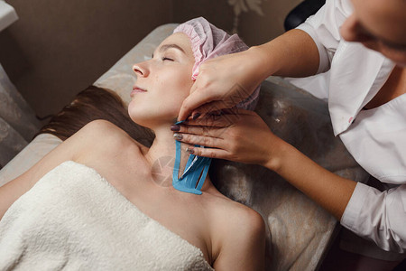 女美容师在家中的桌子上为病人的脸贴上胶带物理治疗和美容程序非手术嫩肤的方法背景图片